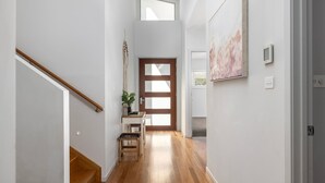 A hallway with wooden flooring, a staircase, a door with frosted glass panels, a small table with a plant, and a wall-mounted artwork. - The Family Tide – large family home, entertaining deck with views, swimming pool, air conditioning (Corlette)