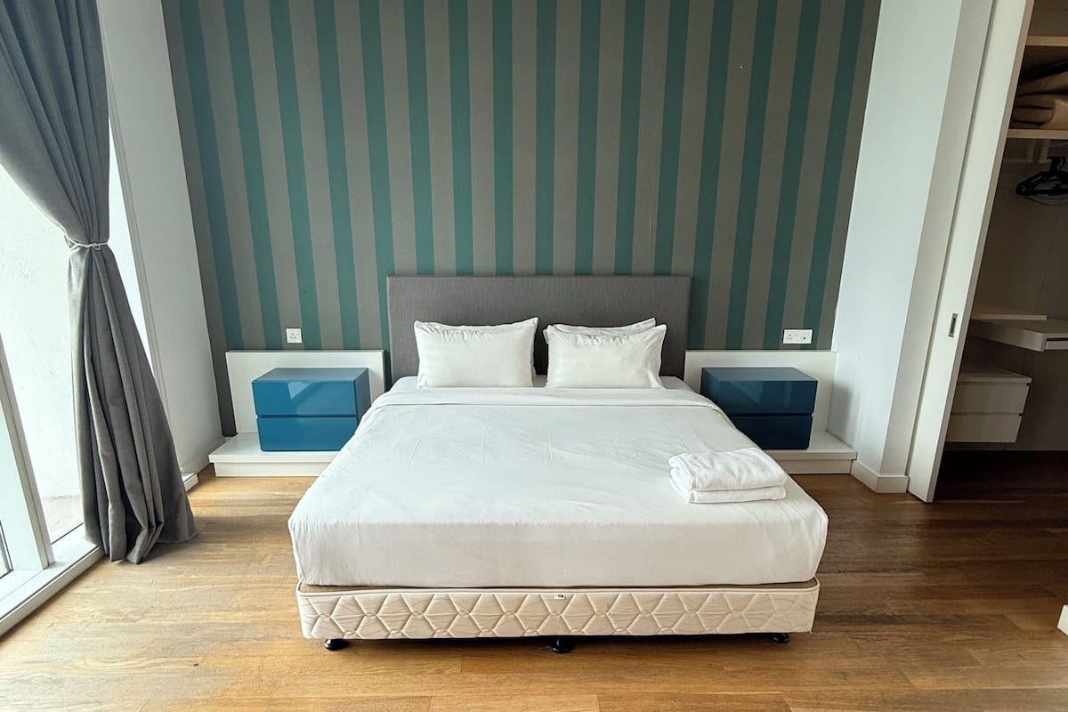 A bedroom with a large bed, two bedside tables, a wardrobe, and a striped wall.