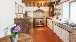 A kitchen with a stone wall, wooden beams, a stainless steel stove, a washing machine, and a sink.