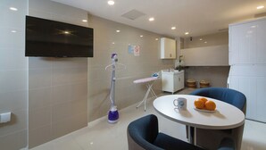 A modern kitchen with a flat-screen TV, a mopping machine, a table with a plate of oranges, and a blue chair. - Huiyue Hotel  (Chengdu)