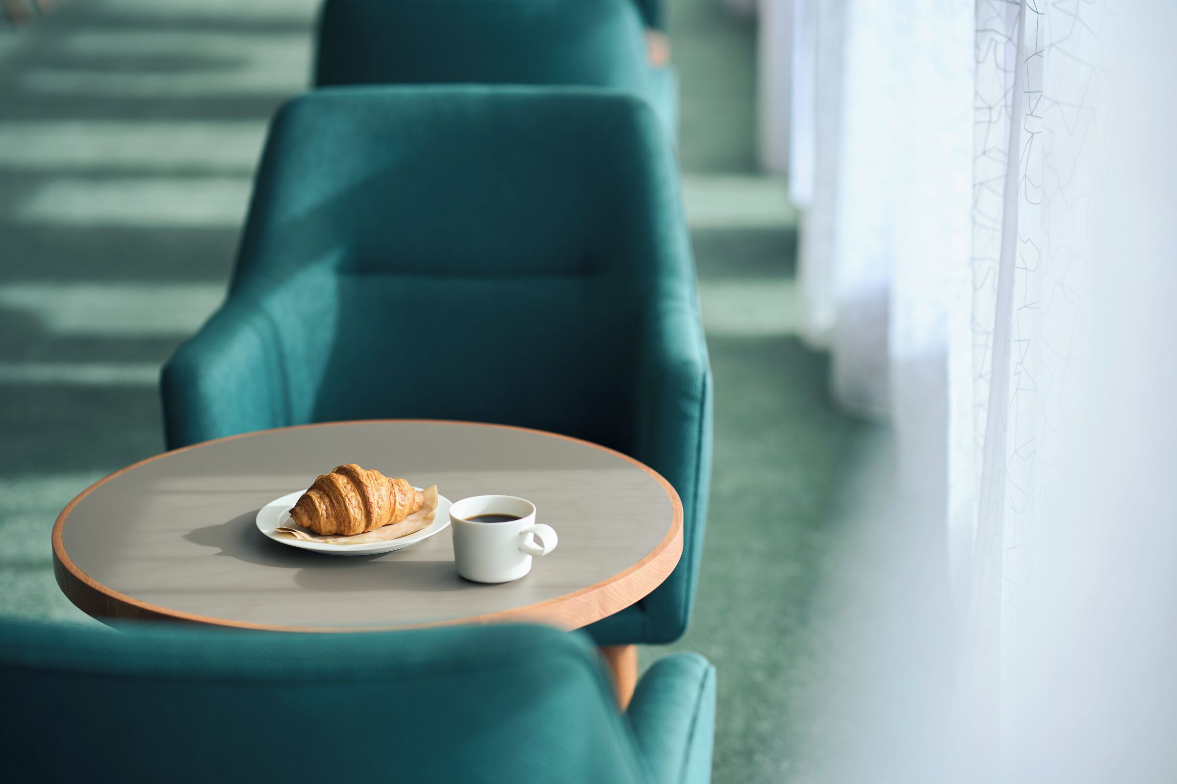 Un coin salon avec des chaises turquoise et une table ronde, un croissant et une tasse de café.