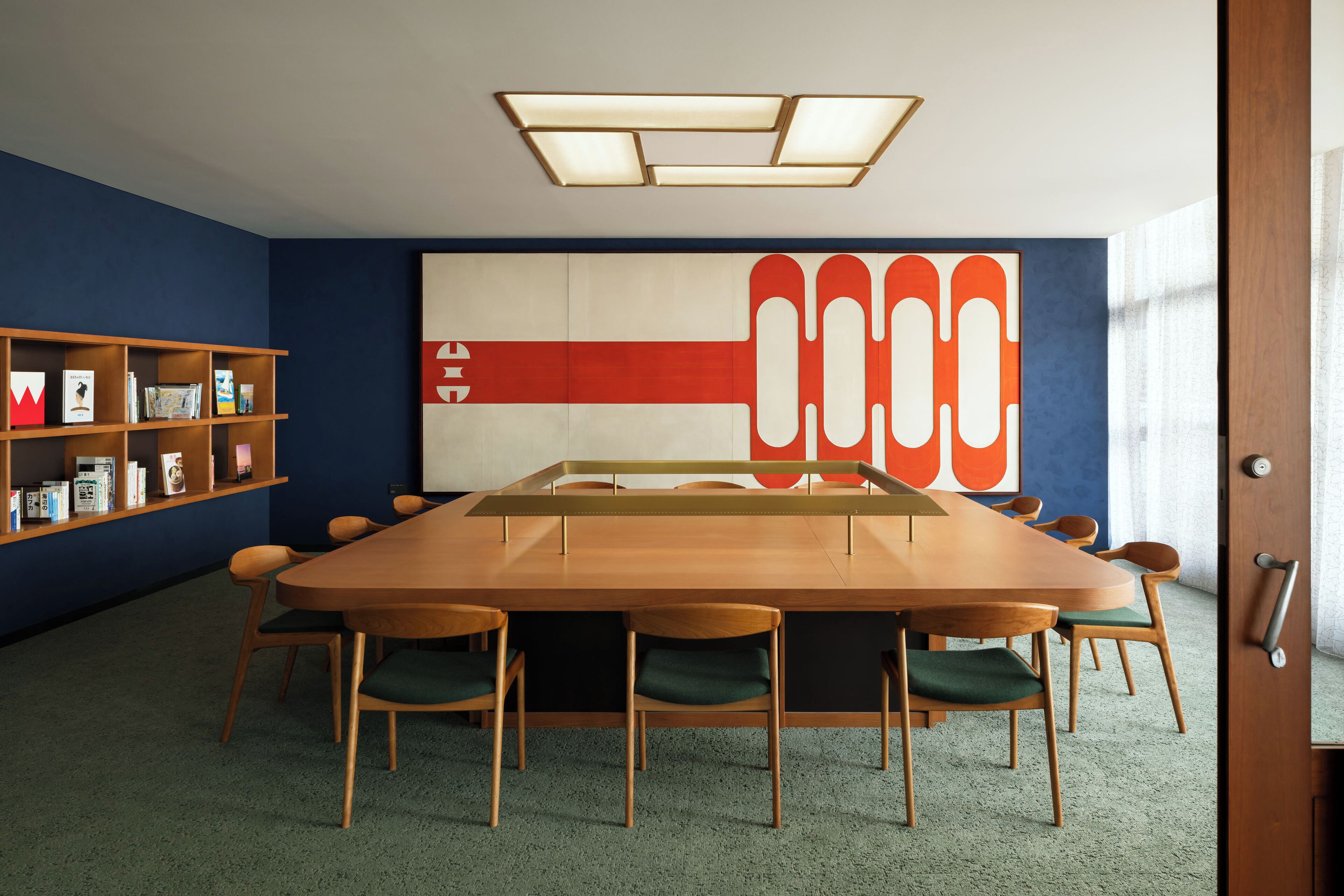 Une salle de conférence avec une longue table, des chaises, une bibliothèque et un grand tableau abstrait accroché au mur.