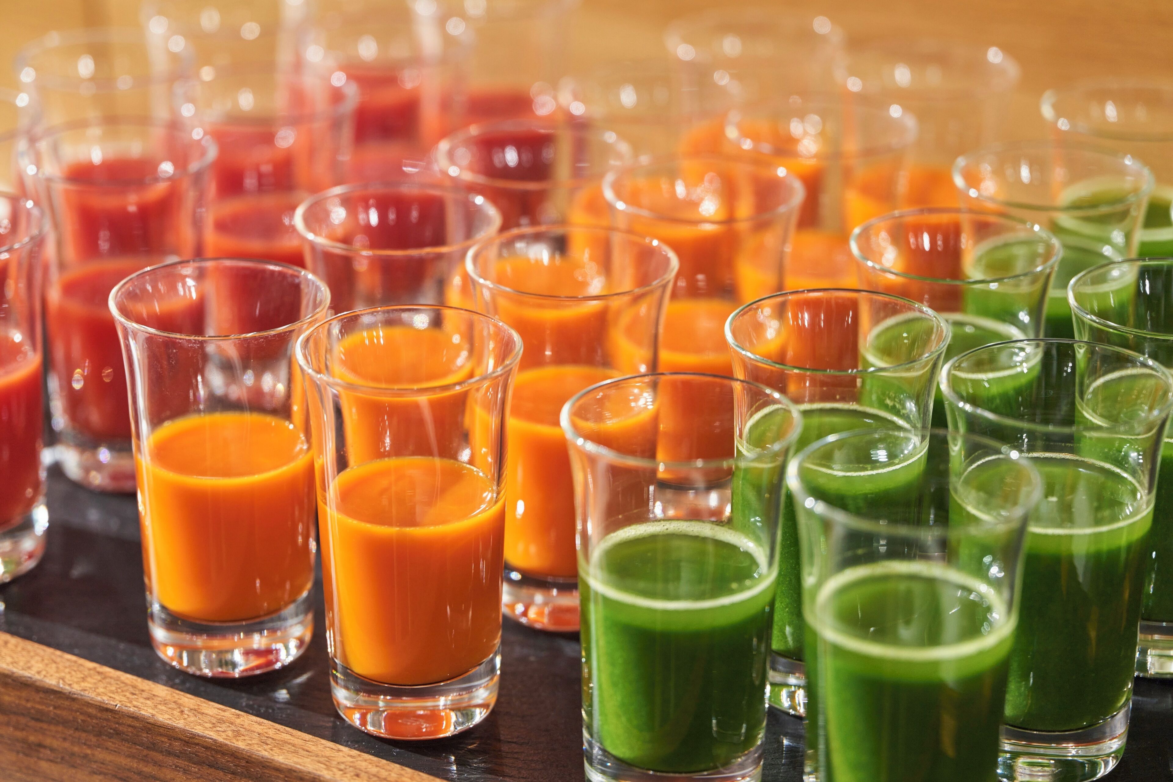 Diversas bebidas coloridas em pequenos copos sobre uma superfície de madeira.
