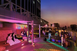 Eine Dachterrasse mit Bühne, Sitzbereichen und einem Klavier.