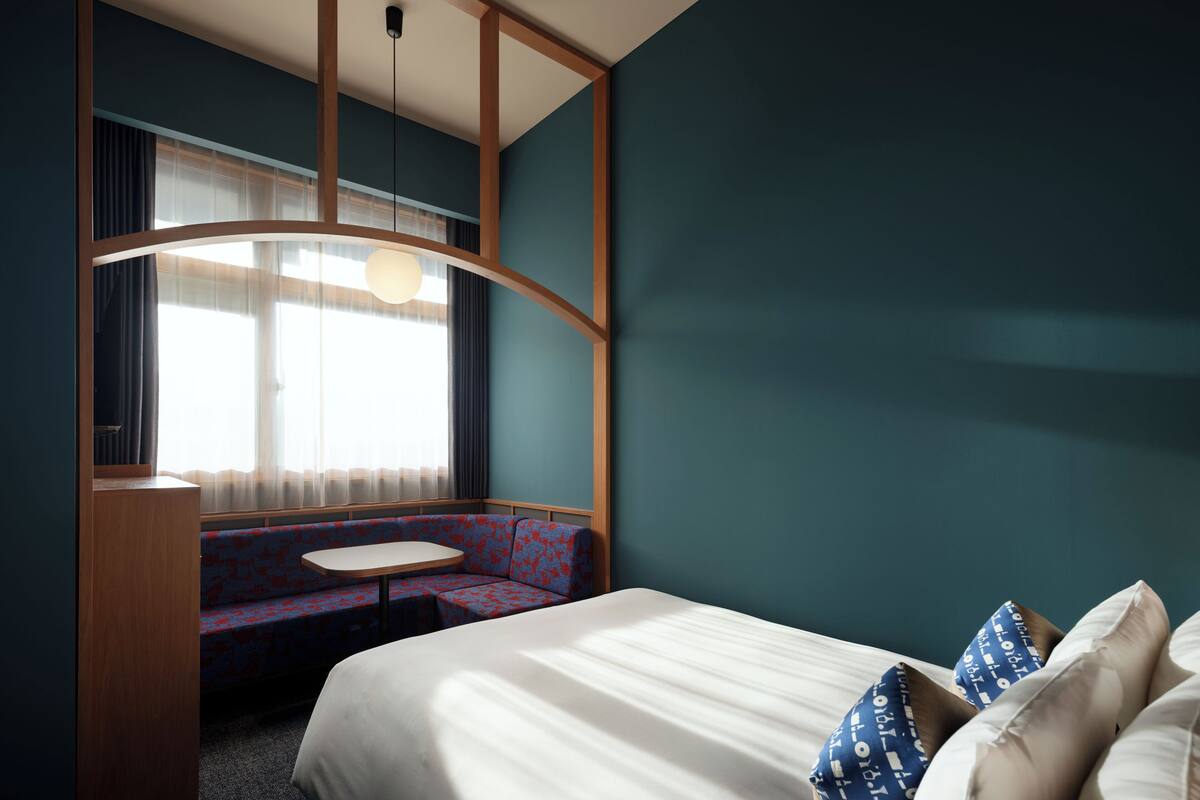 Une chambre d’hôtel avec un lit, une petite table ronde, un canapé et une fenêtre avec des rideaux.