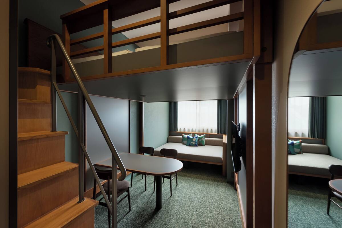 Une chambre d’hôtel avec un lit en mezzanine, un coin repas avec une table et des chaises, et un escalier.