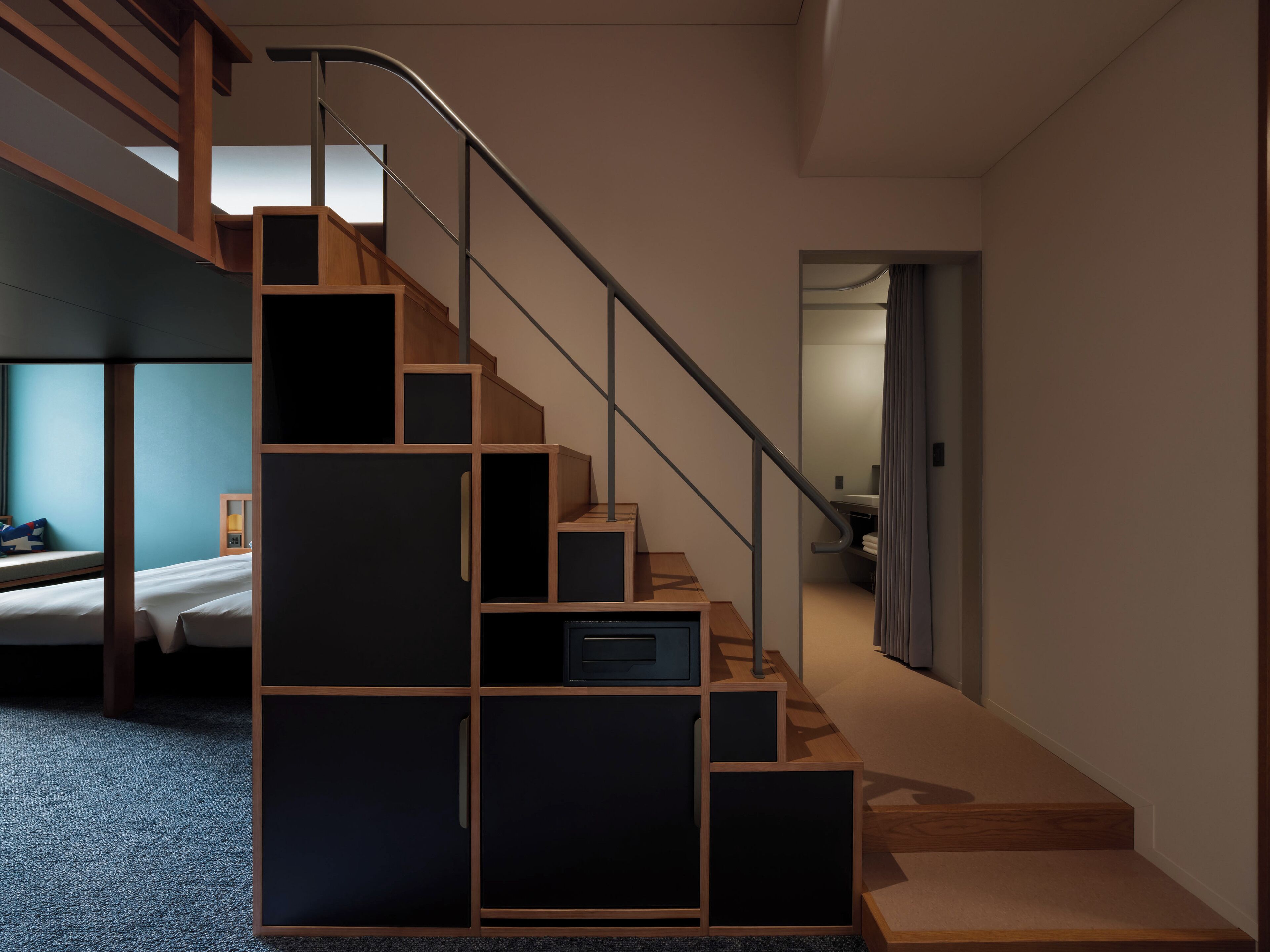 A modern staircase with a wooden finish and metal railings, leading to a bedroom with a bed and a nightstand.