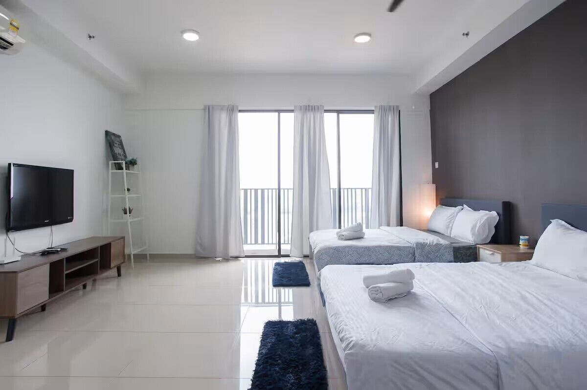 A modern hotel room with a flat-screen TV, a wooden console table, two beds with white bedding, a dark blue rug, and a balcony with curtains.