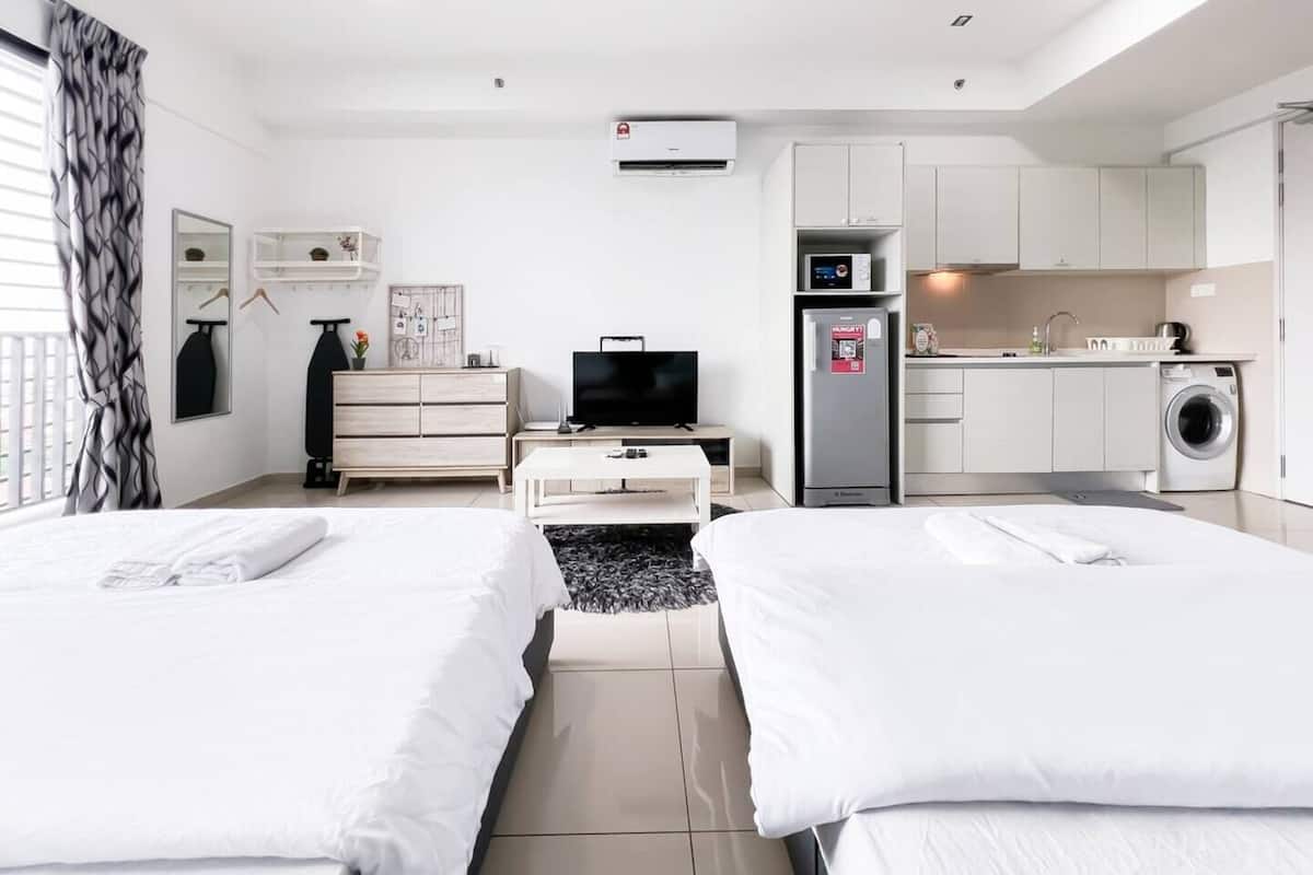 Habitación de hotel con dos camas, televisión, escritorio, lavadora y kitchenette.