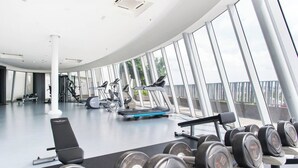 A modern gym with various exercise equipment, large windows, and a clean, spacious layout.