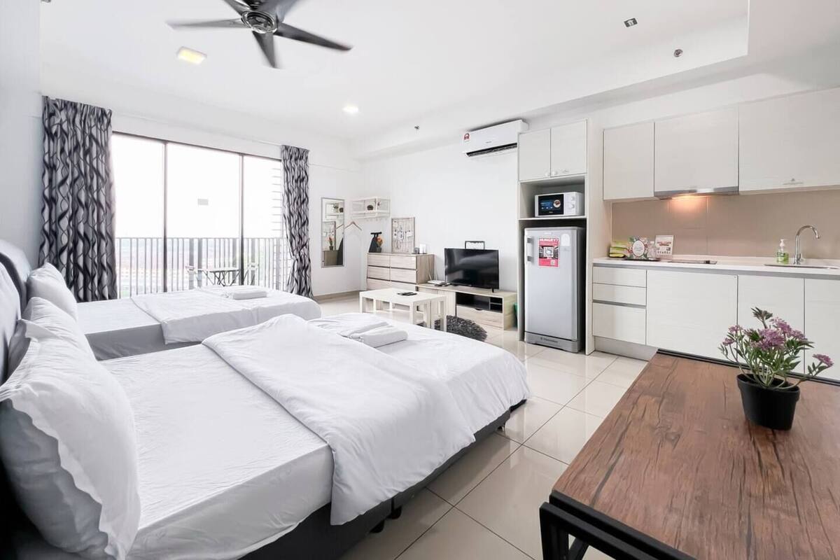 Een moderne hotelkamer met twee bedden, een eettafel, een kitchenette en een balkon met gordijnen.