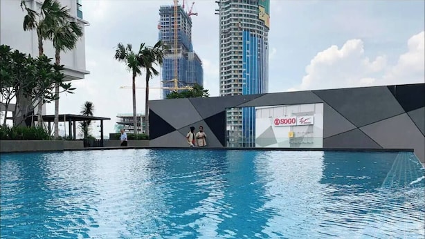 A swimming pool with a modern design, surrounded by palm trees and a cityscape with tall buildings in the background.