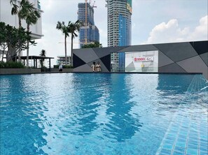 A swimming pool with a modern design, surrounded by palm trees and a cityscape with tall buildings in the background. - ICity Luxury Condo by Smarthome (Shah Alam)