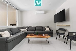 A modern living room with a sectional sofa, a coffee table, a flat-screen TV mounted on the wall, and a sliding glass door.