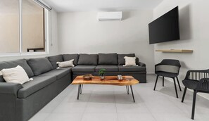 Una sala moderna con un sofá seccional, una mesa de centro, un televisor de pantalla plana montado en la pared y un ventanal corredero.