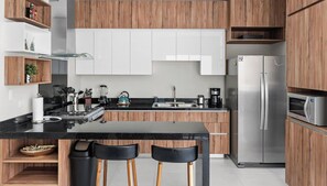 Una cocina moderna con armarios de madera, encimera negra, electrodomésticos de acero inoxidable y una isla central con taburetes de bar.
