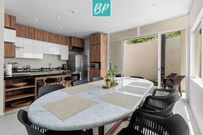 A modern kitchen with wooden cabinets, a marble dining table, and a sliding glass door leading to an outdoor area.