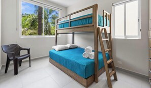 Una cama individual con estructura de madera, una colcha azul y una escalera. Hay una silla y una ventana con vistas a zonas verdes.