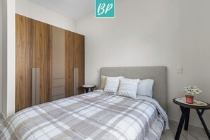 A bedroom with a bed, a nightstand, a small table with a plant, and a wardrobe with wooden panels. - 2BR w/ Pool, Fast WiFi & Beach Gear - Stanza 7 (Bucerías)