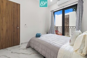 Un dormitorio con cama, armario de madera, balcón con barandilla y vista a un edificio.