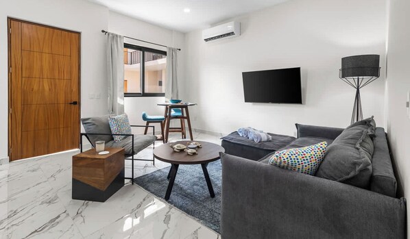 A modern living room with a sofa, a coffee table, a TV mounted on the wall, and a wooden door.