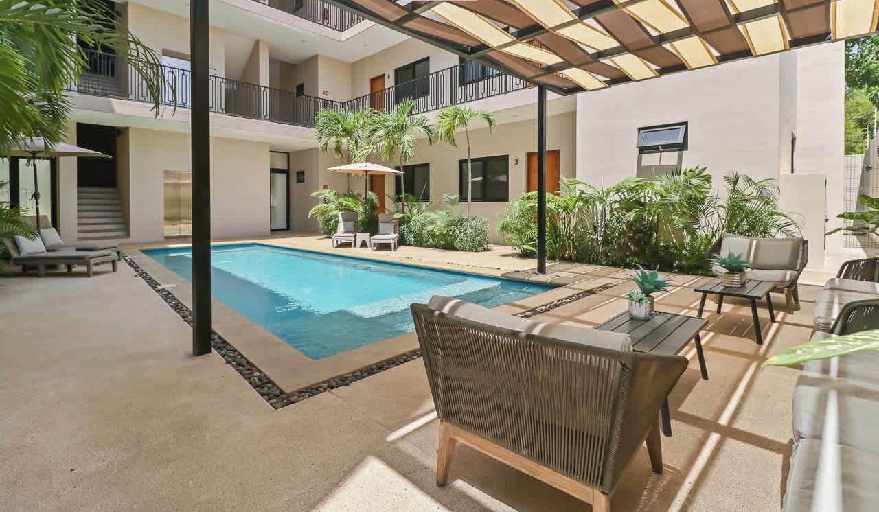 Une cour d’hôtel avec une piscine, des espaces de détente en plein air et de nombreux balcons.