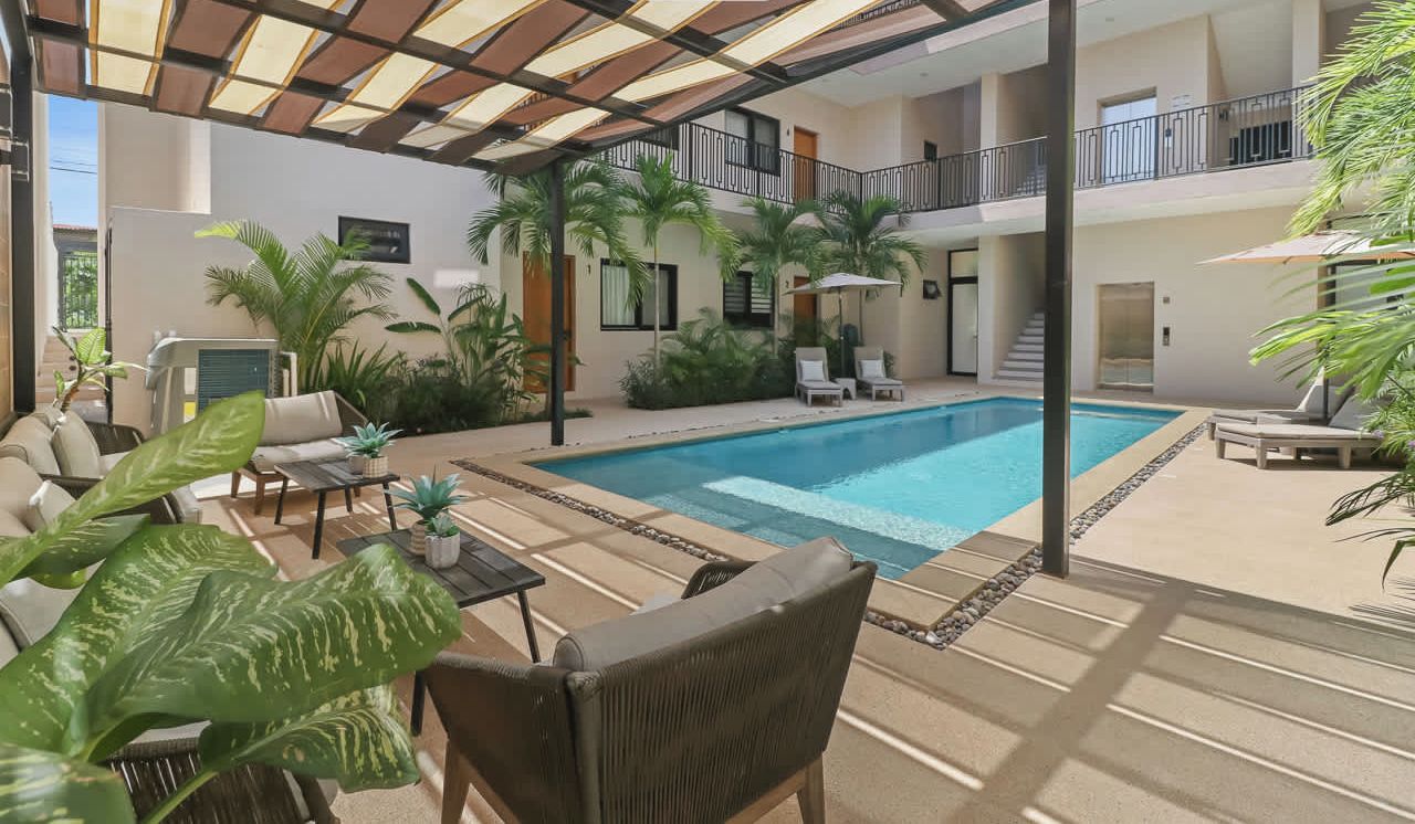A spacious indoor pool area with a covered patio, lounge chairs, and potted plants.