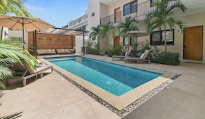 A swimming pool with lounge chairs and umbrellas, surrounded by a building with balconies and palm trees. - 2BR w/ Pool, Fast WiFi & Beach Gear - Stanza 7 (Bucerías)