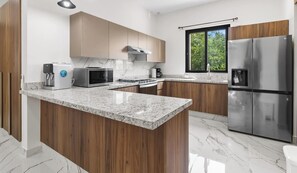 A modern kitchen with wooden cabinets, a granite countertop, stainless steel appliances, and pendant lighting.