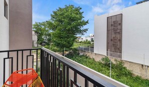 A balcony with a red chair, a tree, and a building with a BP sign. - 2BR w/ Pool, Fast WiFi & Beach Gear - Stanza 7 (Bucerías)