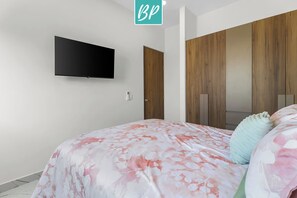 Un dormitorio con cama, televisor montado en la pared, armario de madera y una puerta.