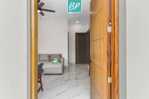 Un couloir avec une porte en bois, un ventilateur de plafond et un canapé avec des coussins.