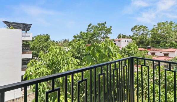 Ein Balkon mit Metallgeländer, der auf einen Garten mit verschiedenen Pflanzen und Bäumen blickt.