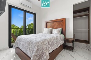 Een slaapkamer met een bed, nachtkastje, kledingkast en een balkon met uitzicht op groen.
