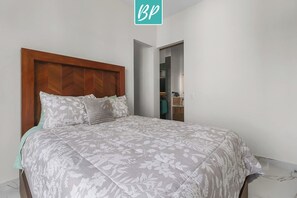 Ein Schlafzimmer mit einem hölzernen Kopfstück, einer zudecke mit Blumenmuster und einem Kleiderschrank mit Spiegel.