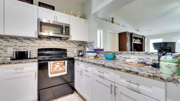 Una cocina moderna con armarios blancos, una estufa negra, un microondas y un salpicadero de azulejos.