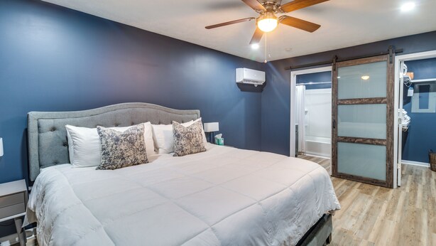 A bedroom with a large bed, a ceiling fan, and a sliding glass door leading to a bathroom. - 7 Mi to Lake Tangipahoa: McComb Home w/ Deck! (McComb)