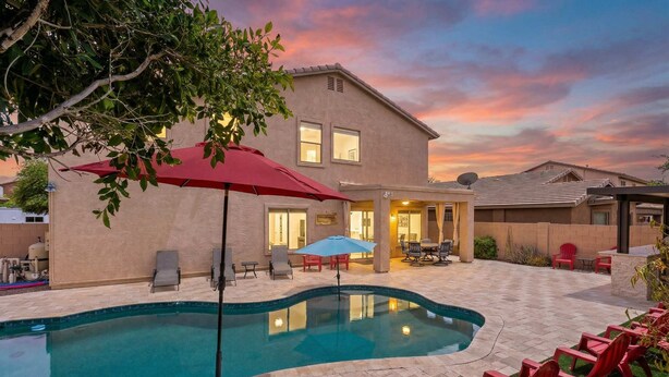 A residential pool area with a house, outdoor furniture, and a sunset sky.