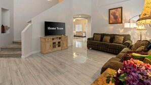 A spacious living room with a flat-screen TV, a sofa, and a staircase.