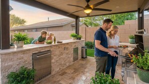 An outdoor kitchen with a built-in grill, a ceiling fan, and potted plants.