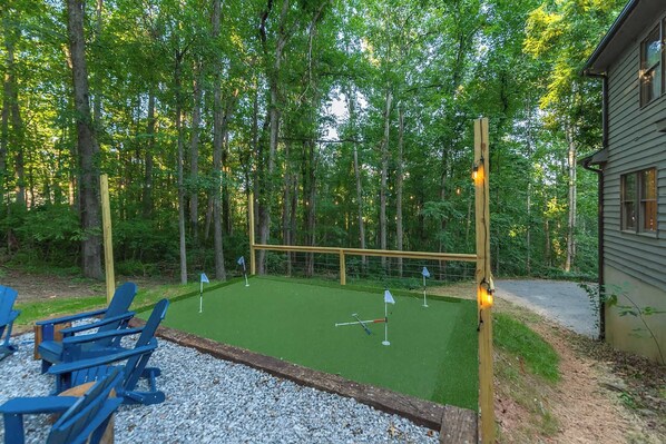 Un campo de mini golf con valla de madera, césped artificial verde y sillas azules.