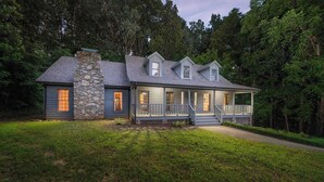 A two-story house with a stone chimney, a porch with railings, and a well-maintained lawn. - 6 Br Sleeps 20 I Sauna•Theater•Putt Putt•Hot Tub (Asheville)