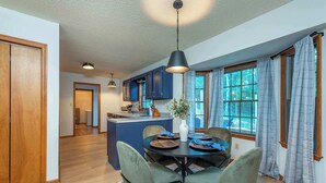 A modern kitchen with blue cabinets, a dining area with a round table and chairs, and a large window with curtains. - 6 Br Sleeps 20 I Sauna•Theater•Putt Putt•Hot Tub (Asheville)