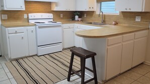 A kitchen with white cabinets, a wooden countertop, a stove, and a sink. - Mid City Modern, Good Vibes in BRLA (Baton Rouge)