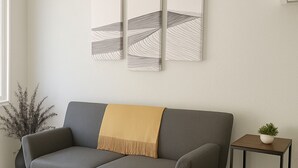 A modern living room with a grey sofa, a small side table with a plant, and abstract wall art. - Bright Studio Retreat in Chico (Chico)
