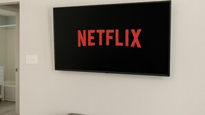 A television mounted on a wall with a Netflix logo, a grey bench below, and a wooden floor. - Bright Studio Retreat in Chico (Chico)