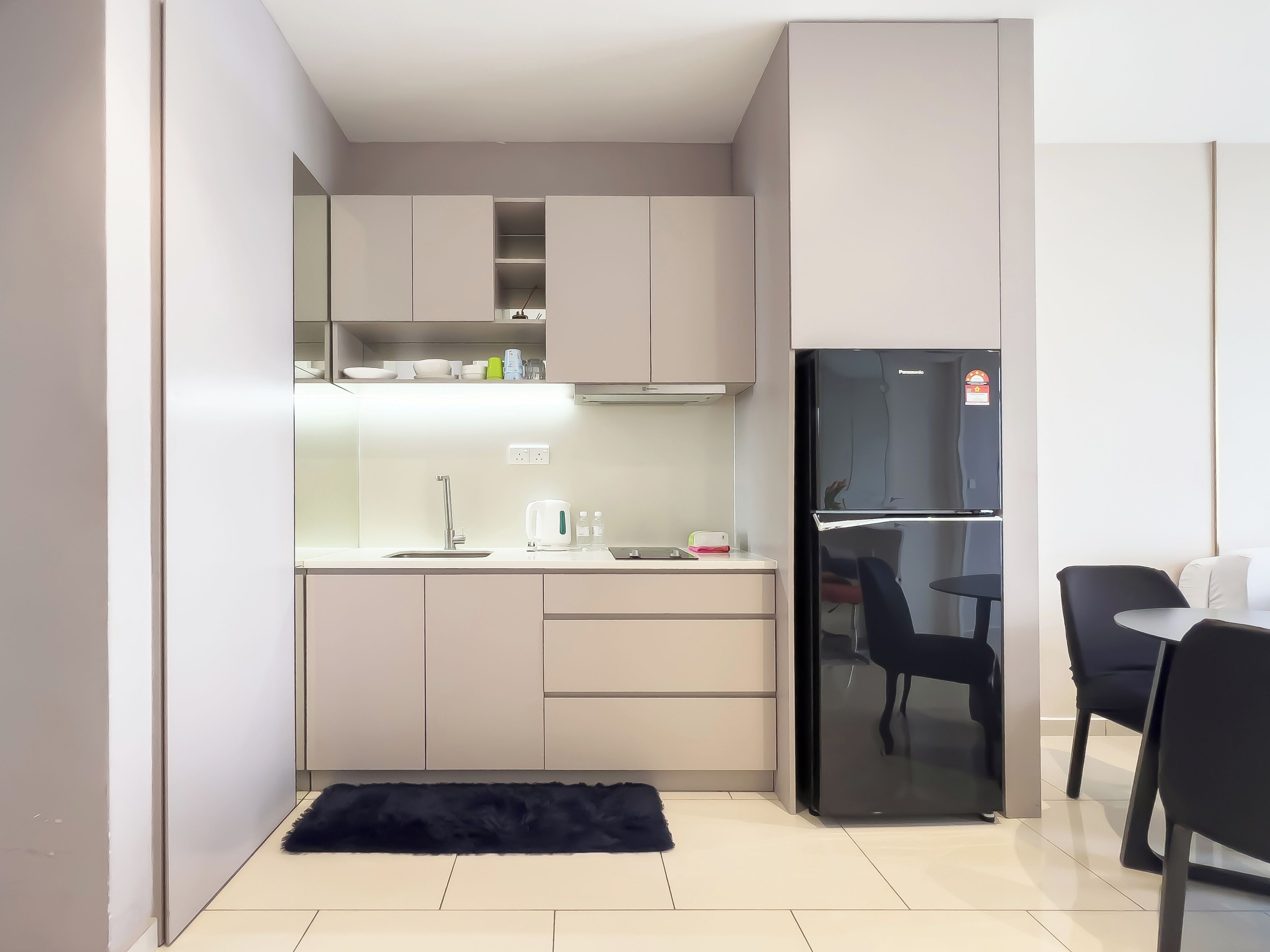 Cocina compacta con refrigerador, lavamanos y una zona de comedor con sillas.