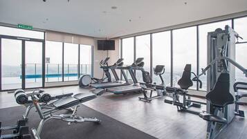 A gym with cardio machines, weightlifting equipment, and large windows offering a city view.