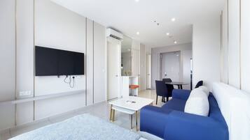 A modern hotel room with a large bed, a TV mounted on the wall, a small table, and a seating area with chairs.