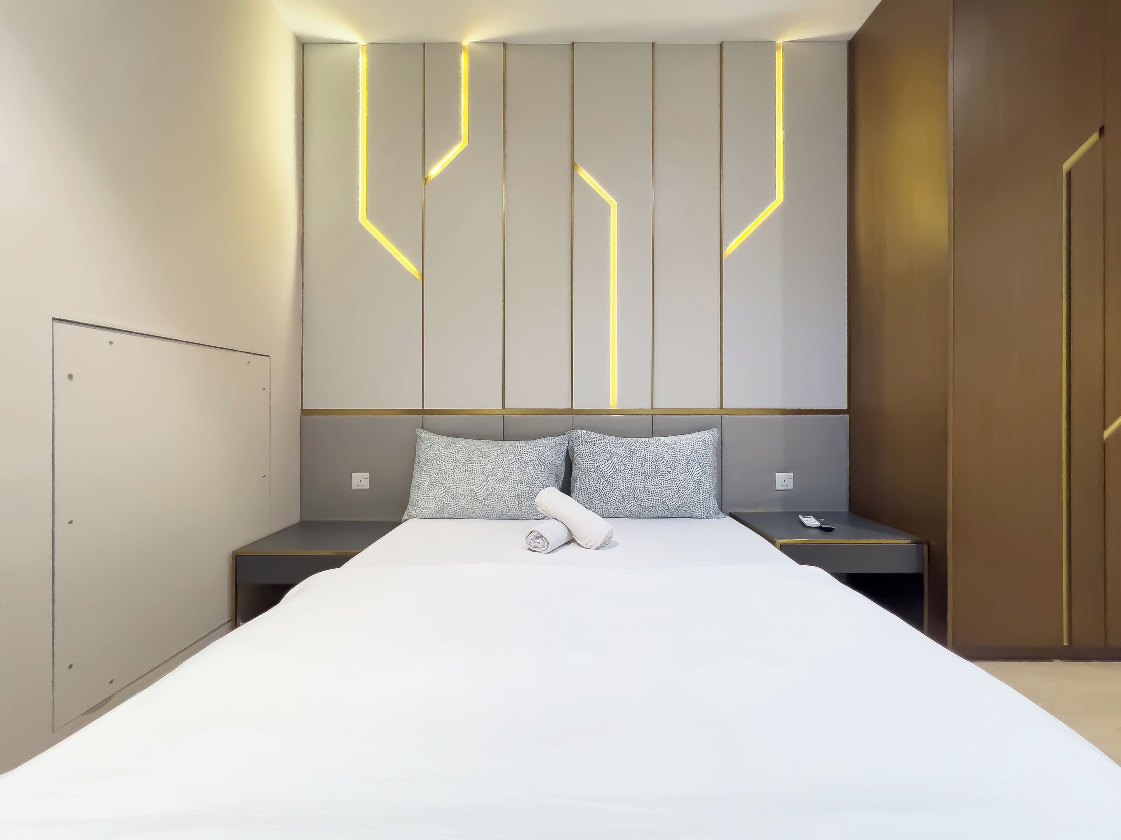Une chambre d’hôtel moderne avec un grand lit, deux tables de chevet et une tête de lit ornée de motifs lumineux.
